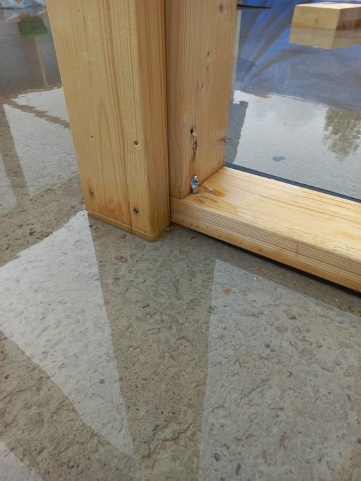 Närbild av ett träregelverk med en skruv vid dess hörn, mot en polerad betonggolvbakgrund.