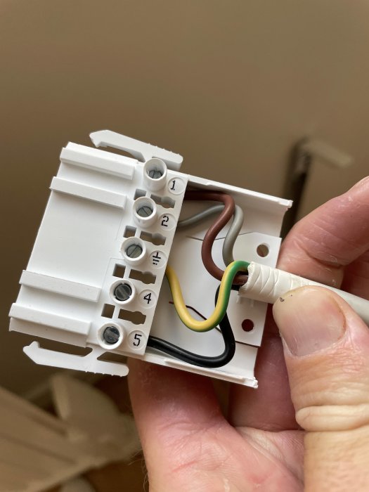 Hand håller en elektrisk strömbrytare med synliga kabelanslutningar.