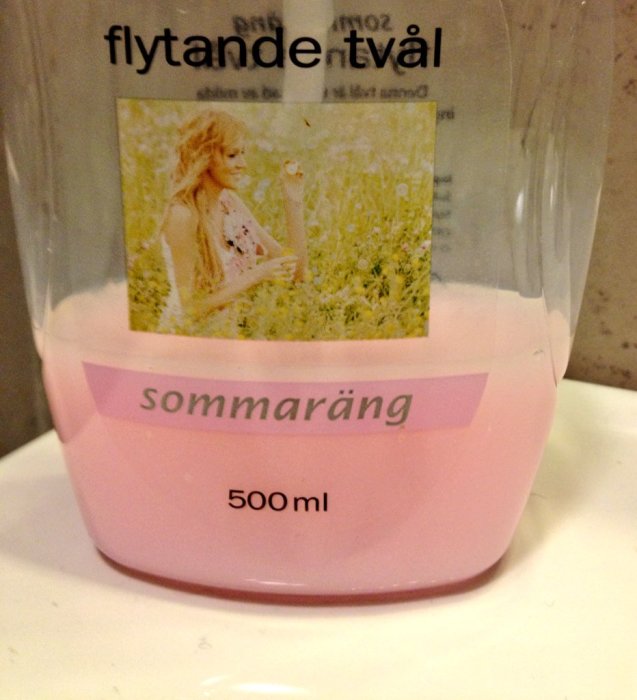 Flaska med rosa flytande tvål märkt "sommarrång", med bild av kvinna i blomsteräng.
