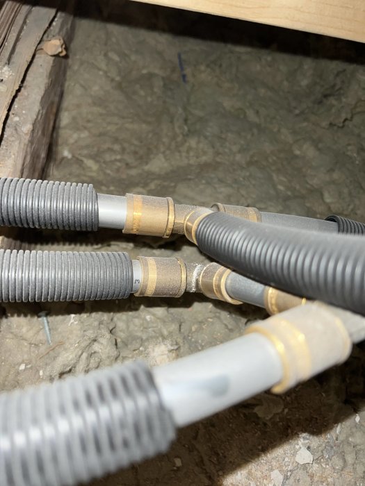 Elektriska kablar i flexibla rör och mässingsfästen, dragna i en crawl space under golv.