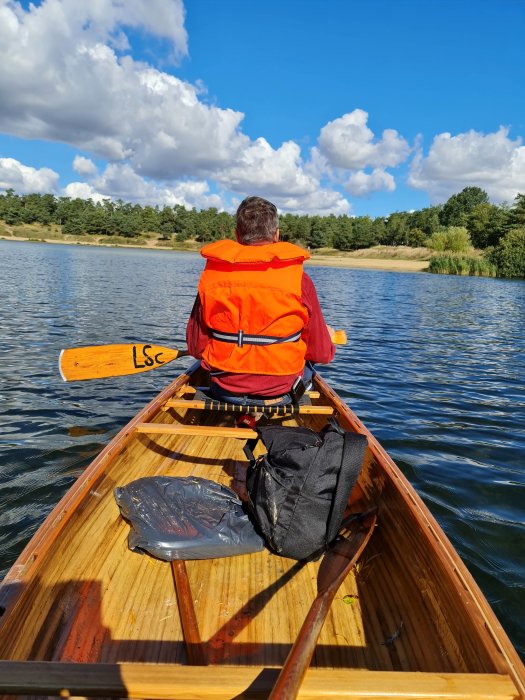 Person i orange flytväst som paddlar en träkanot på en sjö en solig dag.