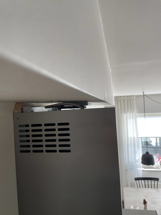 En köksfläkt installerad under ett snedtak med synlig ventilation och kök i bakgrunden.