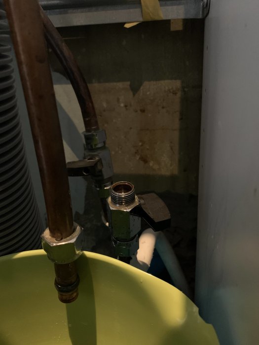 Vattenledningar och en ventil nära en grön skål med synlig vattendroppe.