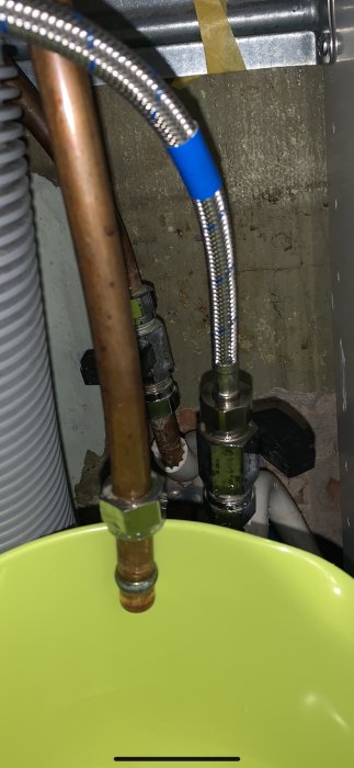 VVS-installation med kopparledningar och flexibel slang ovanför grön hink.