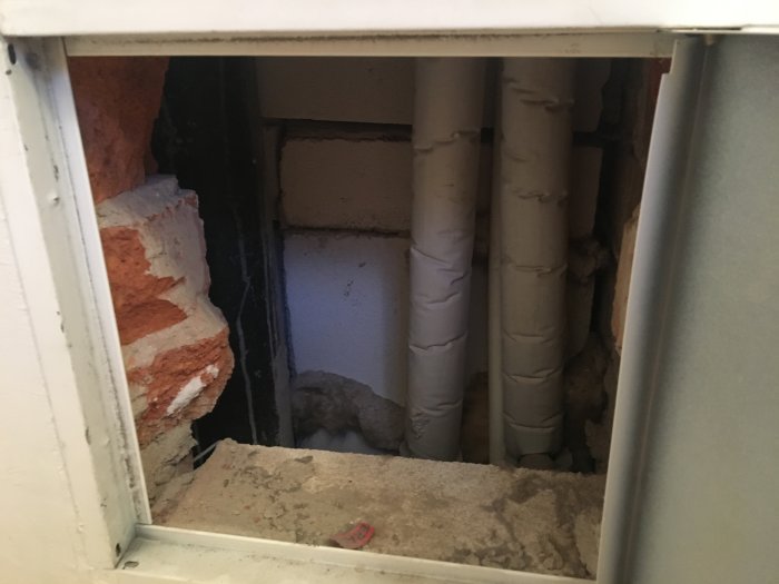 Öppning i vägg visar rör och murade tegelstenar under renovering.