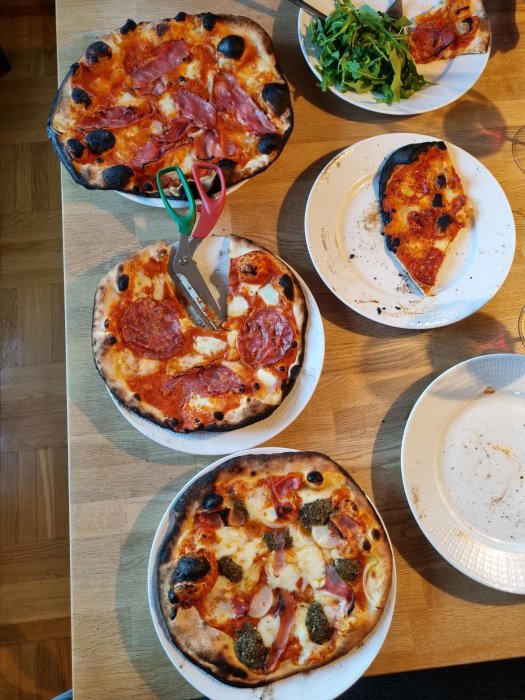 Tre hembakade pizzor på bordet, varav en är delvis äten, med olika toppings och brända kanter.