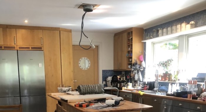 Kök under renovering med borttagen köksfläkt, verktyg på bänk och öppna elledningar i taket.