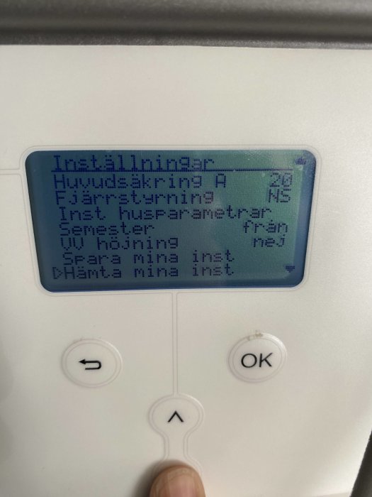 Finger justerar inställningar på en uppvärmningsanläggningens kontrollpanel med visad text på skärmen.