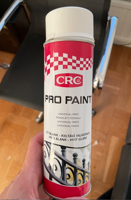 Ett handhållet sprayburk av CRC PRO PAINT i fokus med text på svenska, finska och norska om vit högblank färg.