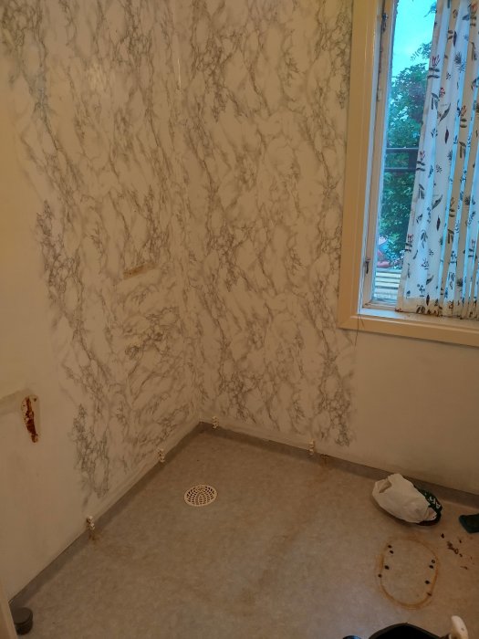 Ett hörn av ett rum under renovering med mönstrad tapet och fönster med gardiner.