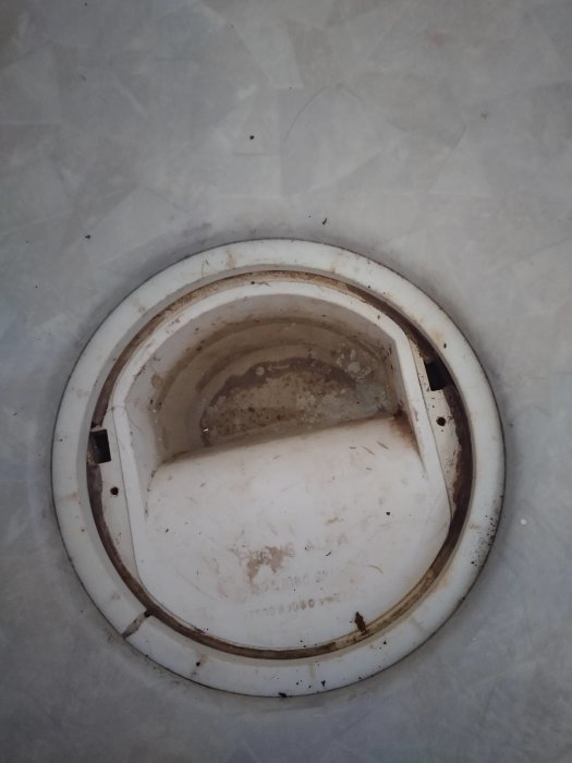 Smutsig vit avloppsfälla i ett badrum, i behov av rengöring eller byte.