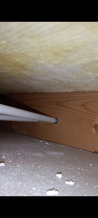 Isolering och kablar nära träbjälke i ett pågående byggprojekt, med synligt sågspån på golvet.