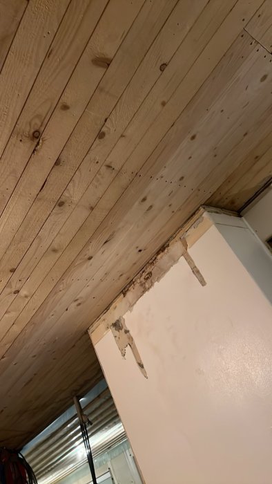 Ny monterad råspont i taket nära en plats med skadat gipstak och vägg.