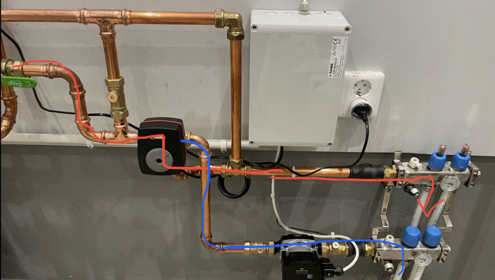 Installation av golvvärmesystem med kopparledningar, fördelare, shunt och cirkulationspump på vägg.