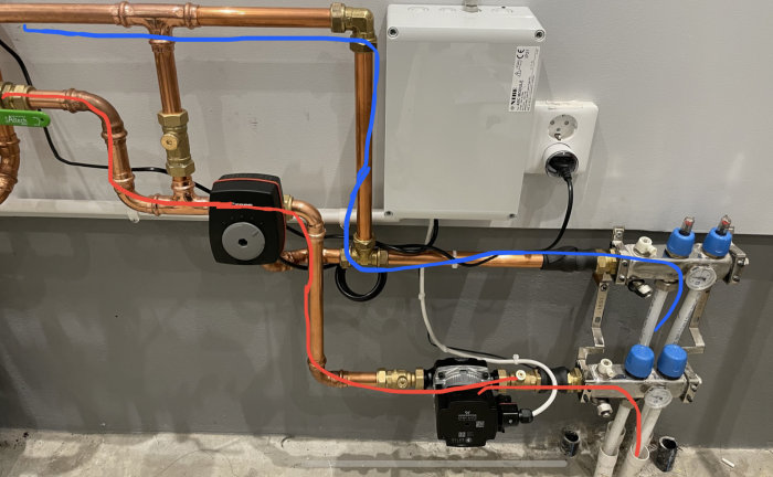 Installation av golvvärmesystem med kopparledningar, cirkulationspumpar och fördelare mot en vägg.