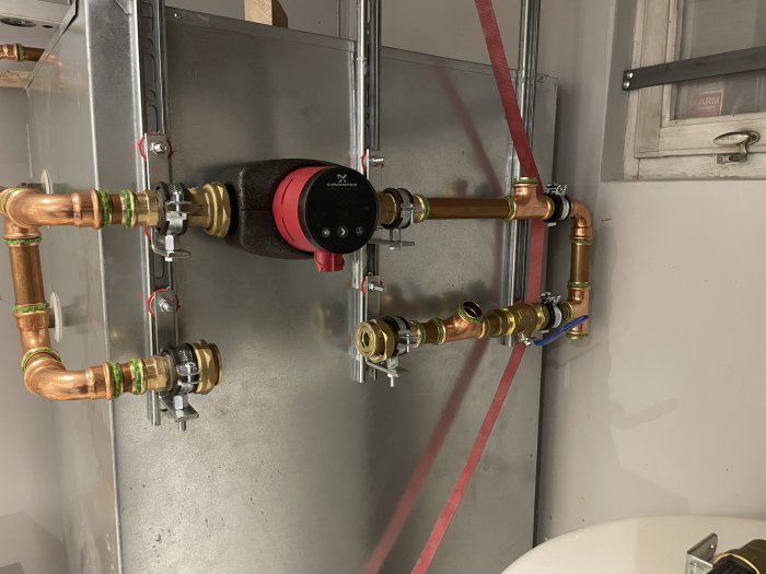 Installationsbild av upphängda rör och kopplingar med cirkulationspump för värmesystem, fästa i tak med Flamco ClickEasy system.