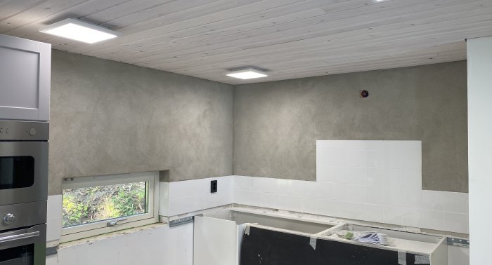 Renoverat kök halvfärdigt med spacklade väggar, vit kakelvägg och inbyggd belysning.
