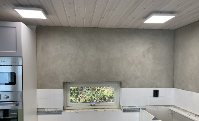 Ett kök under renovering med väggar putsade av grannen, vita kakelplattor och en träpanel i taket.