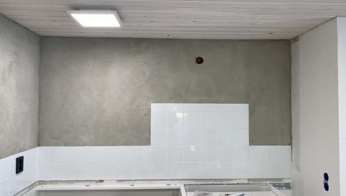 Kök under renovering med vit kakel och träpanel i taket, oavslutad vägg och elektriska uttag.