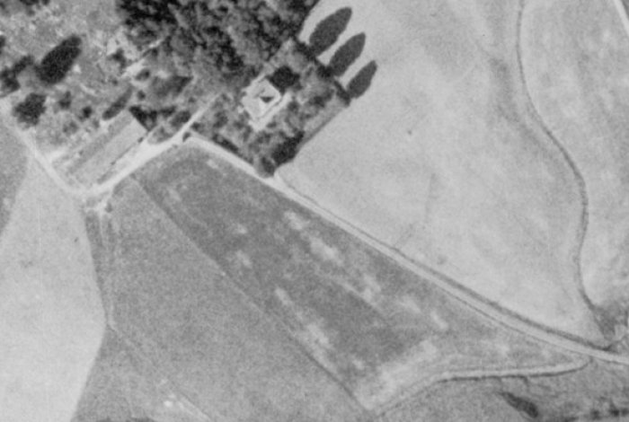 Svartvit flygbild från 60-talet med en krökt väg vid en gård, innan ombyggnation till rak väg.