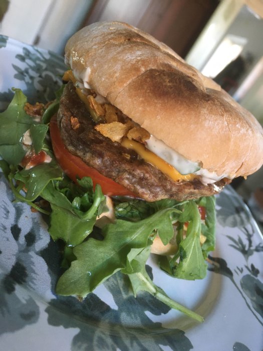 Laddad hamburgare med sallad och flera såser på ett mönstrat fat.
