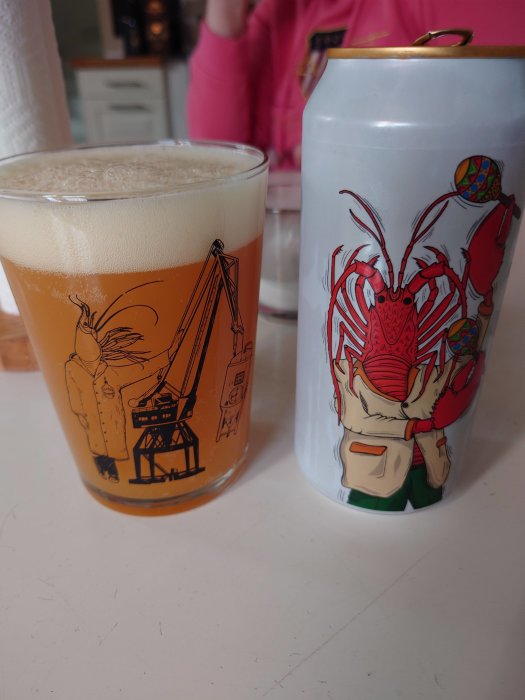 Ett glas öl vid sidan av en ölburk med kräftdesign, båda med konstnärliga illustrationer.