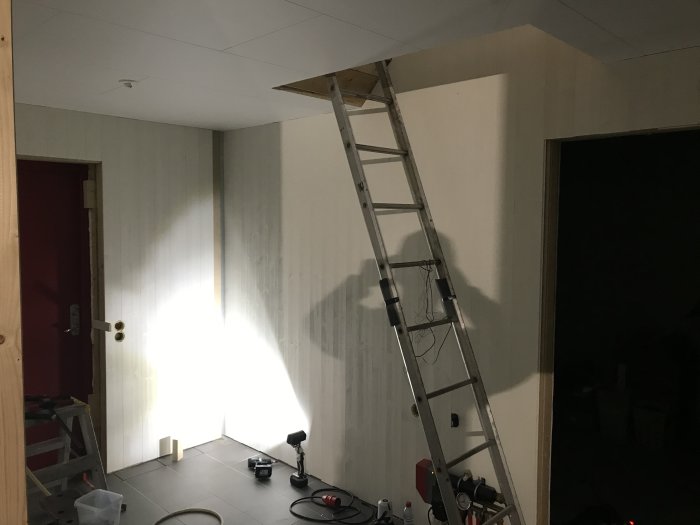 Inomhusbild av en hall under renovering med nymonterad vit panel på väggarna och en stege lutad mot väggen.