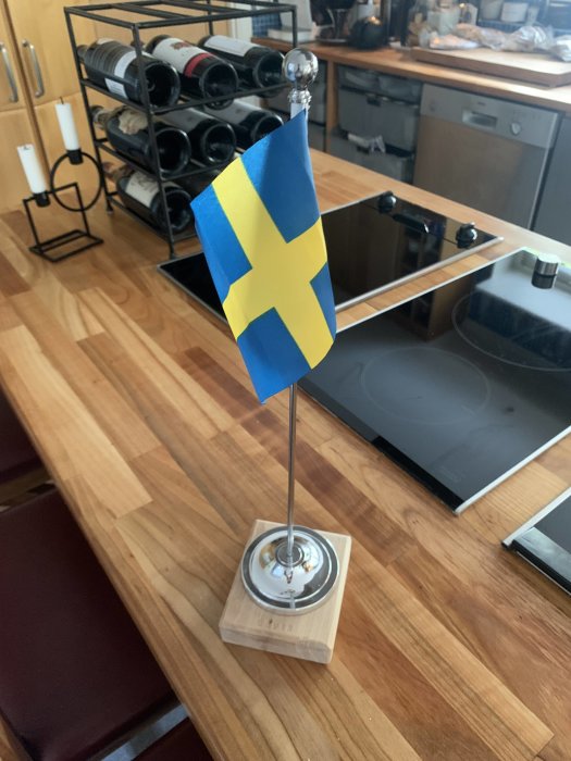 Svensk flagga på pinne med silverkula på toppen, monterad på träfot med tillhörande metallbeslag.