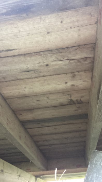 Undersidan av en träbjälklag i ett byggprojekt med synliga grova träbjälkar.