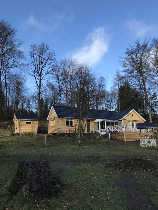 Nybyggt trähus med veranda och solpaneler, omgivet av träd och en friggebod.