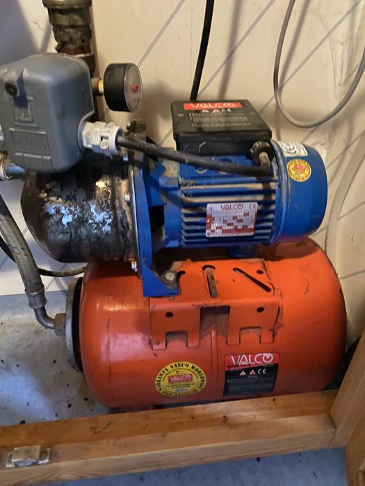Röd och blå Valco-kompressor med motor och lufttank placerad i ett garage.