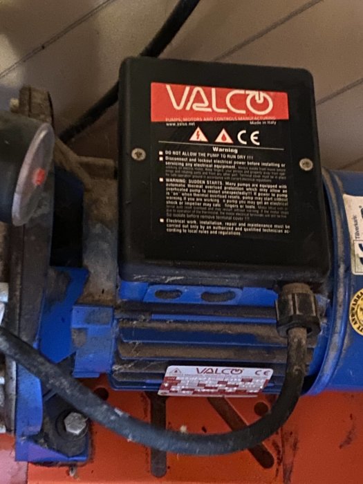 Valco-pump monterad på en maskin med varningsetiketter och CE-märkning, synligt damm och slitage.