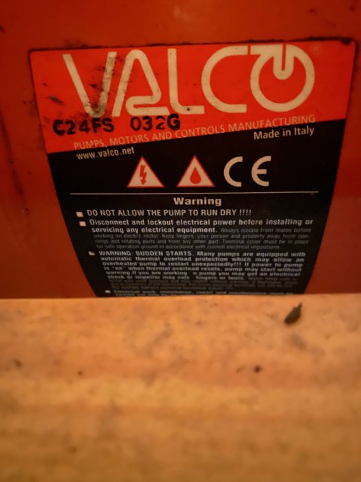 Närbild på en varningsetikett från VALCO med instruktioner och varningssymboler, monterad på en orange yta.