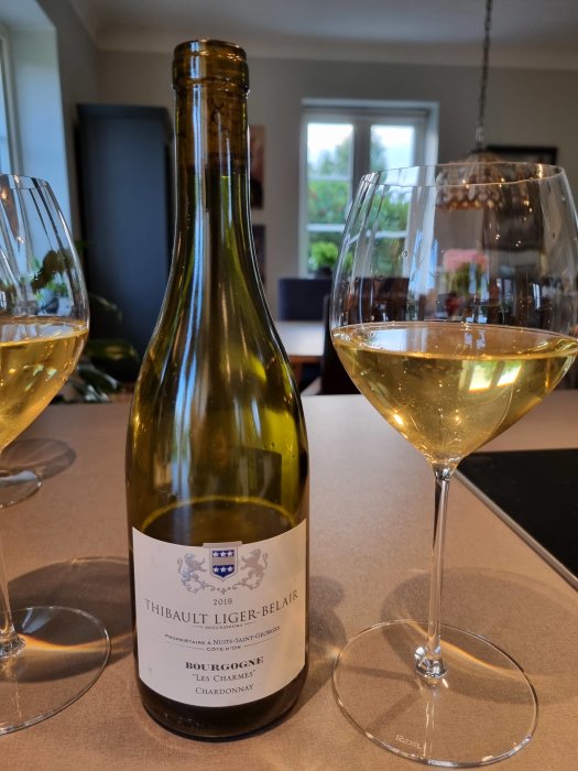 Flaska bourgogne-chardonnay med två vinglas, ett delvis fyllt, på bord.