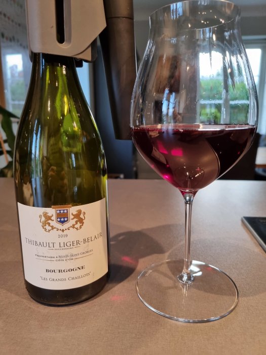 Bourgogne-vinflaska med etiketten "Thibault Liger-Belair 2019 Bourgogne Les Grands Chaillots" bredvid ett glas med rödvin.