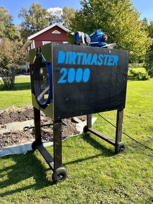 Självtillverkad jord- och kompostsikt vid namn "DIRTMASTER 2000" på hjul i en trädgård.