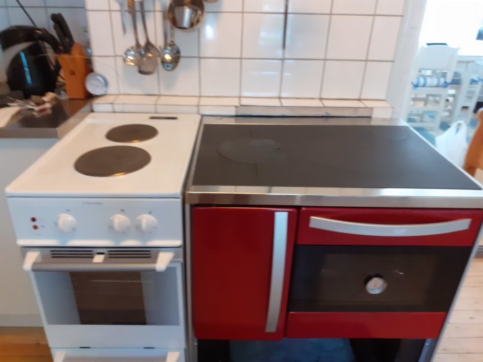 Gammal vit spis bredvid en modern svart induktionshäll med röda skåpluckor.