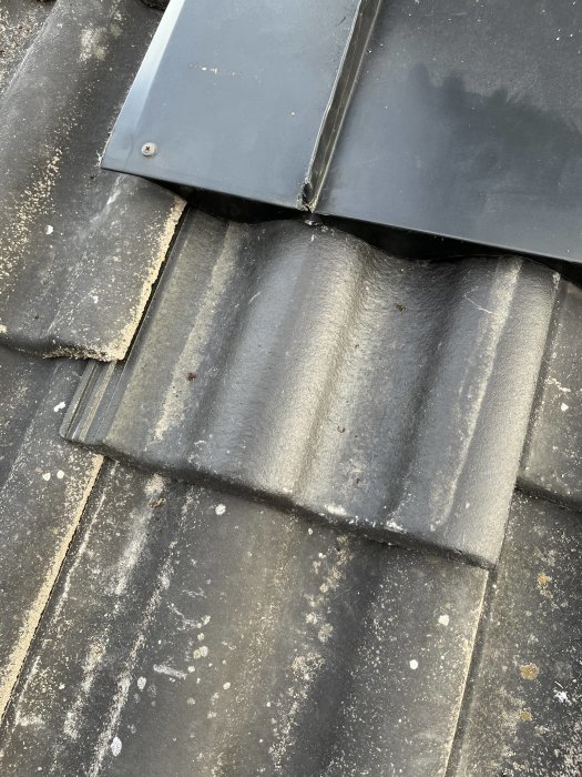 Modifierad plåt vid skorsten med skruvar på ett tak av svarta takpannor.