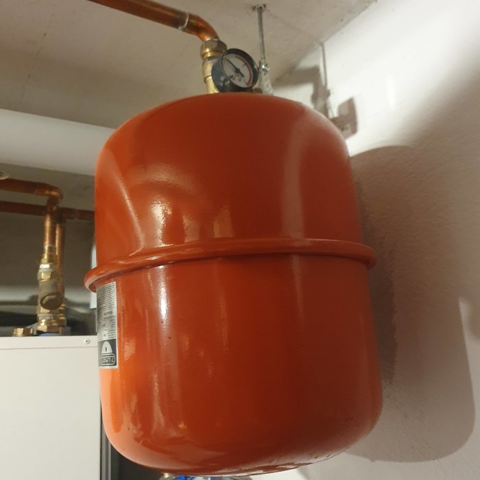 Orange expansionskärl för vatten med manometer installerat i ett tak.