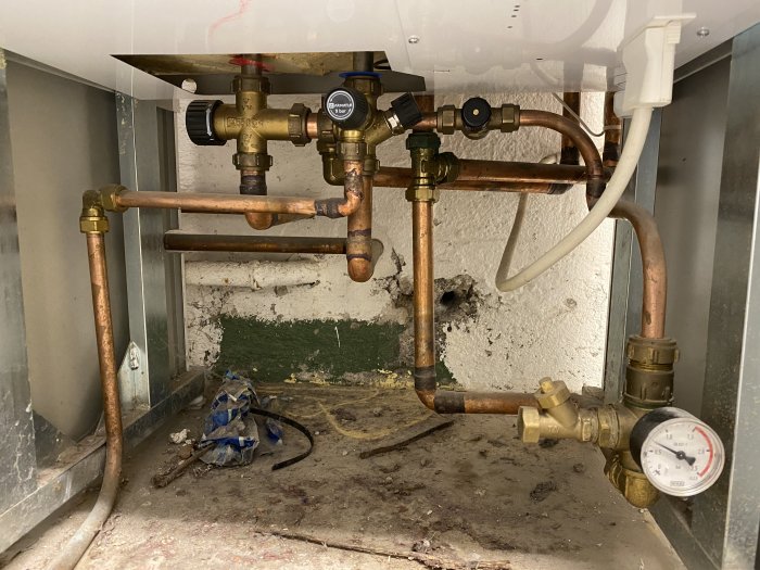 VVS-installation under diskbänk med kopparledningar, ventiler och tryckmätare.