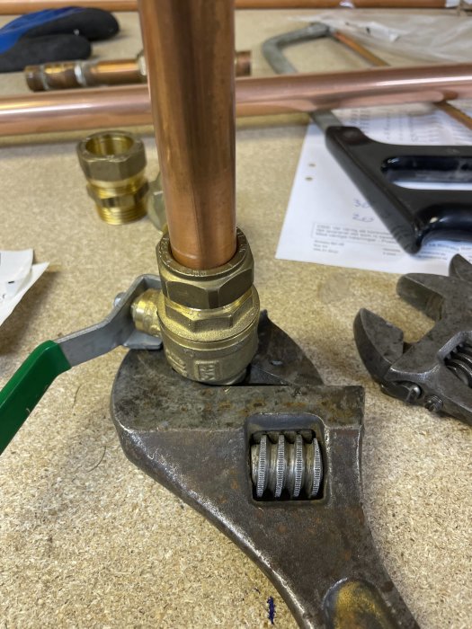 Närbild av ett kopparrör med en nyinstallerad klämkoppling och en kulventil, verktyg syns i bakgrunden.