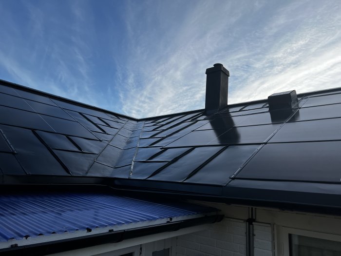 Solpaneler installerade på ett hus med svarta Sunroof-plattor, skorsten och blå himmel i bakgrunden.