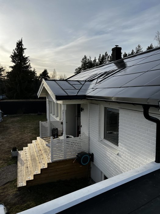 Hus med soldrivet Sunroof-system och en nybyggd träterrass, i skymningen.