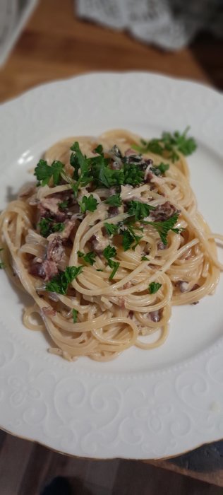 En tallrik carbonara med spaghetti, bacon och persilja på en vit tallrik.