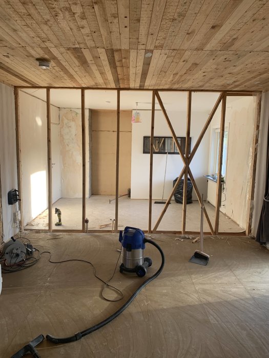 Renoveringsarbete i rum med oskyddade spånskivor, en träkonstruktion och en golvdammsugare.