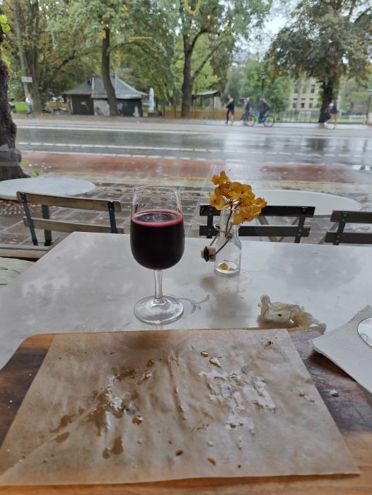 Ett glas rött Lambrusco-vin på bordet framför en tom tallrik, med utsikt över regnig gata.