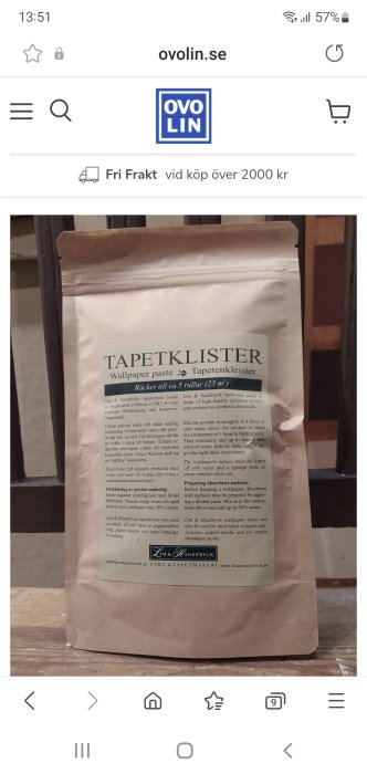 Påse med tapetklister står på ett träbord, instruktionslabel med text och logotyp synlig.