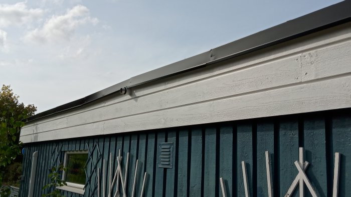 Detalj av takfot och hängränna på ett blått trähus med vit panel