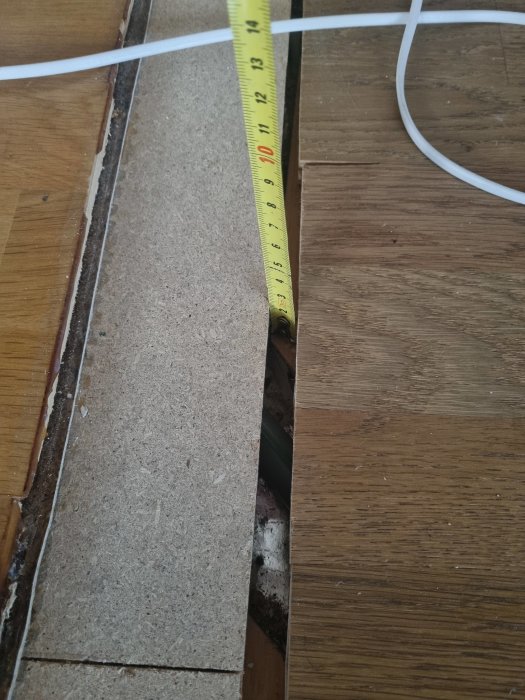 Måttband visar gapet mellan golvbrädor under renovering.