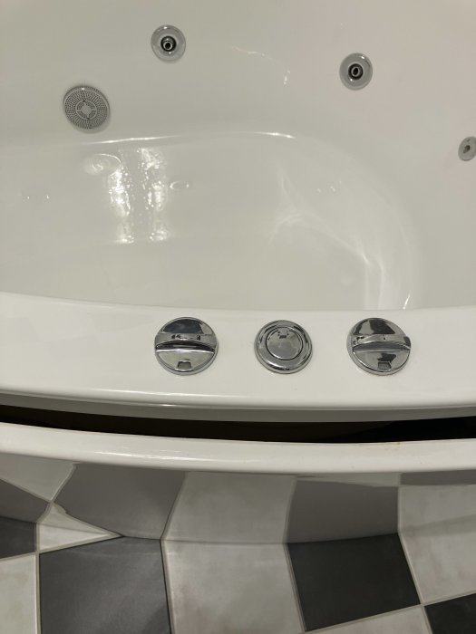 Närbild av ett rent badkar med tre kromade vred och ett dräneringshål.